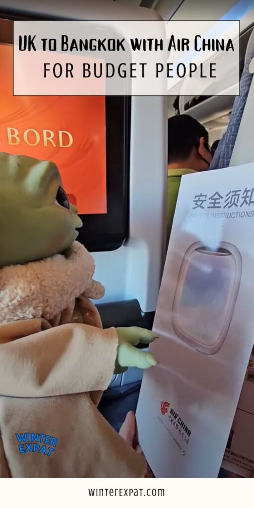 A vertical close-up shot inside an airplane cabin showing a Grogu (Baby Yoda) plush toy positioned as if looking at an Air China safety instructions pamphlet. In the background, an inflight entertainment screen glowing orange with the text "BORD" is partially visible. A translucent text box at the top reads "UK TO BANGKOK WITH AIR CHINA FOR BUDGET PEOPLE", with the WinterExpat logo in the bottom left and "WINTEREXPAT.COM" printed along the bottom white border. Original photo by Ariana of WinterExpat.