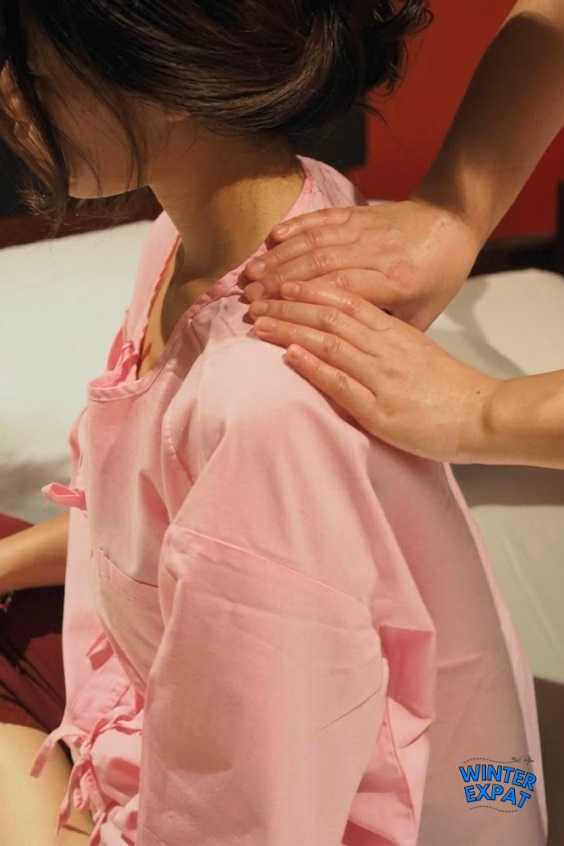 A therapist performs a seated shoulder massage on Ariana during a treatment session at Health Land Spa in Bangkok. Original photo by Ariana of WinterExpat.