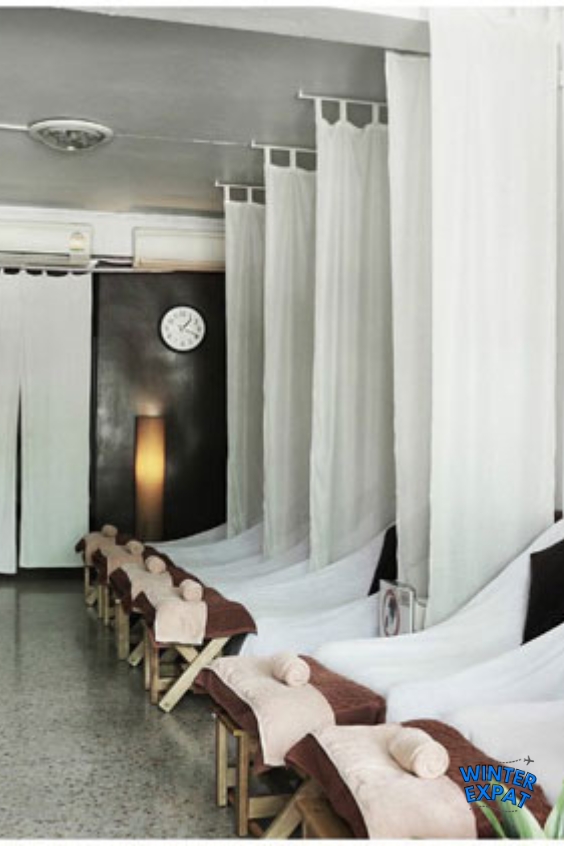 A row of neatly prepared massage beds separated by white curtains inside Zen Tara Massage & Spa in Bangkok. Original photo by Ariana of WinterExpat.
