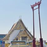 Wat Suthat temple with the Giant Red Swing standing in front under a clear blue sky in Bangkok, Thailand. Original photo by Ariana of WinterExpat.