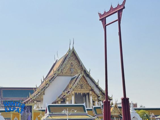 Wat Suthat temple with the Giant Red Swing standing in front under a clear blue sky in Bangkok, Thailand. Original photo by Ariana of WinterExpat.
