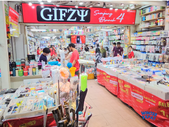 Shoppers browsing inside the brightly lit GIFZY wholesale stationery and novelty gift shop at Sampheng Market in Bangkok. Original photo by Ariana of WinterExpat.